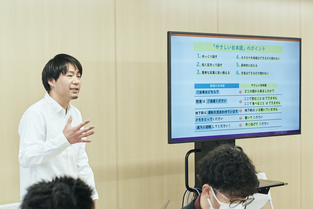 タキザワさんがモニターの横でやさしい日本語のポイントについて説明している