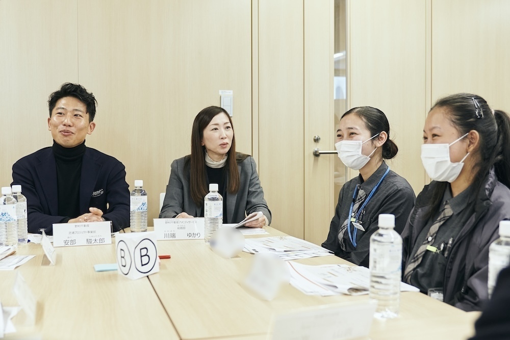 ワークショップのテーブルで、日本人の男女社員2人と外国人ワーカーの女性2人が笑顔で話している