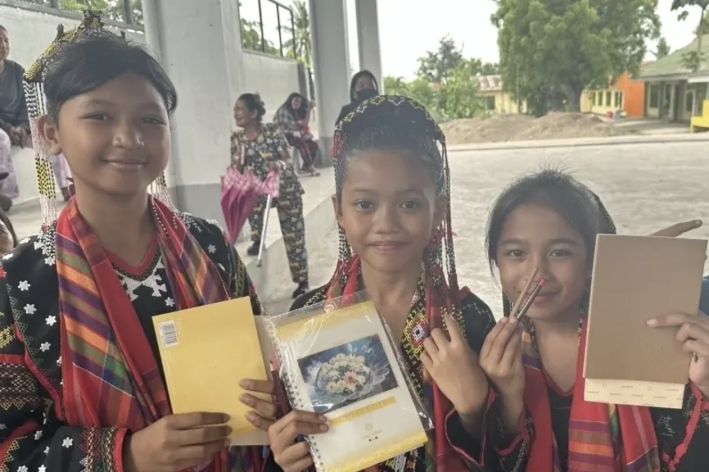 寄付された文具を手に持ち笑顔を見せている3人の少女