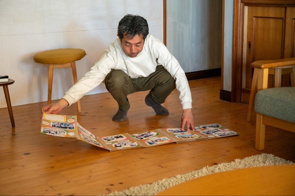 床に広げた写真入りの冊子を見ている中川さん