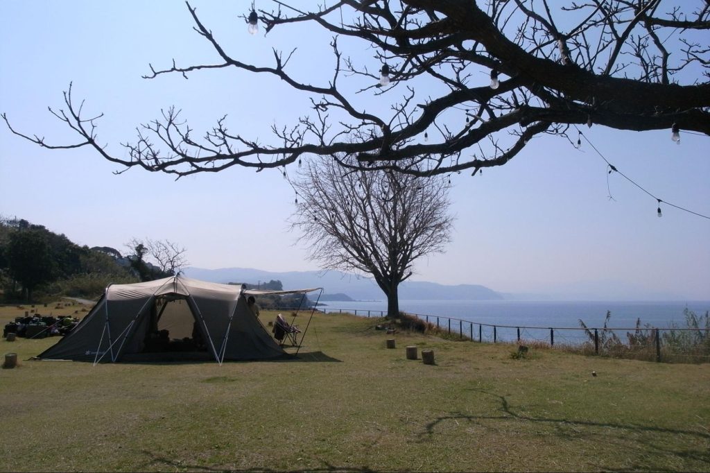 海沿いの芝生広場に設営された大型テントとアウトドアチェア