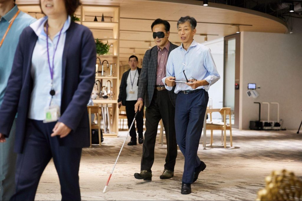白杖を持った芳賀コーポレート統括が、ガイド役の声掛けを受けながらオフィス内を歩行体験している様子