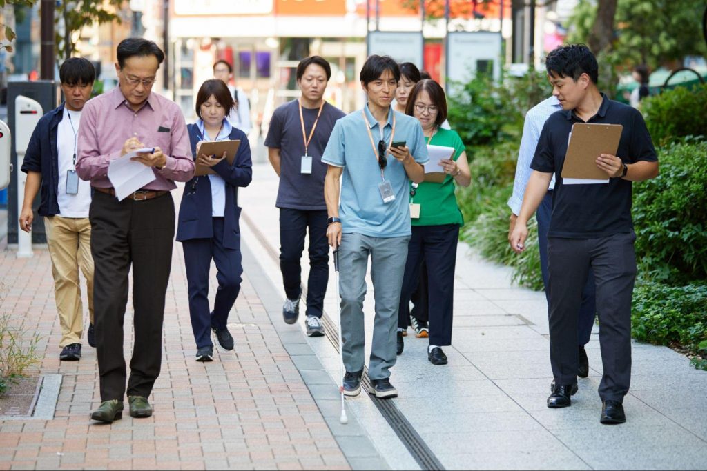 街なかを歩きながら、言葉の道案内を聞き取りつつメモを取る参加者たちのフィールドワークの様子