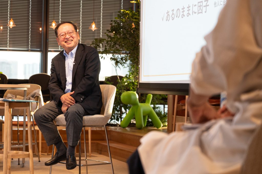 新井CEOが椅子に腰かけ、笑顔で対談に応じる様子