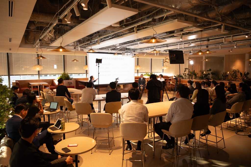 Participants seated at tables, listening to the speakers and viewing the screen at the front.