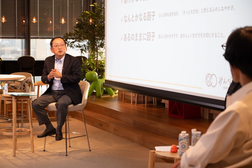 CEO Arai seated and speaking with his hands together, with Mr. Ohata shown in the foreground.